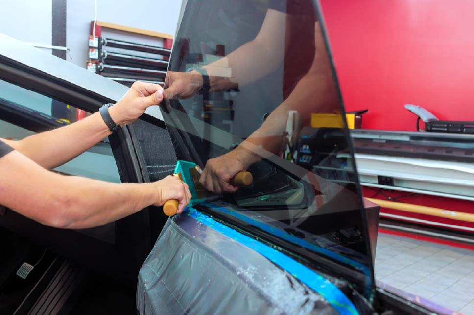 A man tinting the rear windows of a red car.